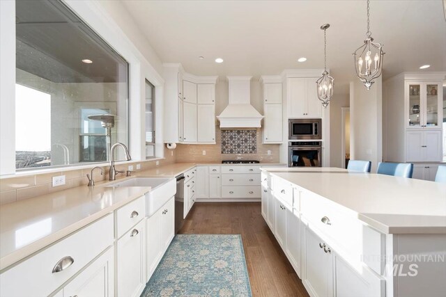 kitchen featuring custom range hood, decorative backsplash, stainless steel appliances, white cabinetry, and a sink