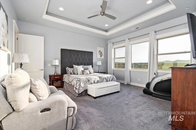 carpeted bedroom featuring a tray ceiling, baseboards, visible vents, and a ceiling fan