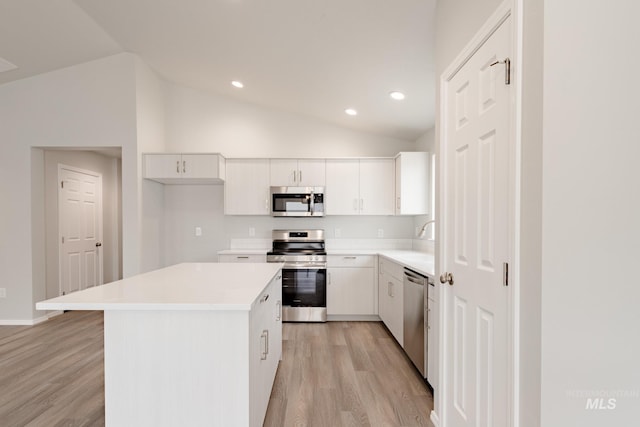 kitchen with light wood-type flooring, light countertops, white cabinetry, appliances with stainless steel finishes, and vaulted ceiling