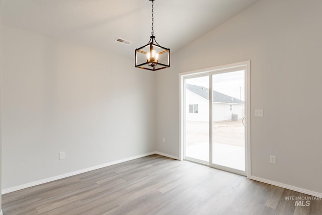 empty room featuring a notable chandelier, light wood-style floors, baseboards, lofted ceiling, and visible vents