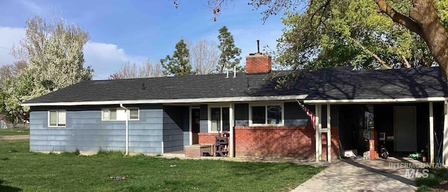back of property featuring a lawn, brick siding, roof with shingles, and a chimney