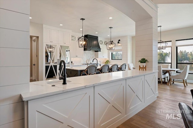 kitchen with tasteful backsplash, premium range hood, light hardwood / wood-style floors, white cabinetry, and hanging light fixtures