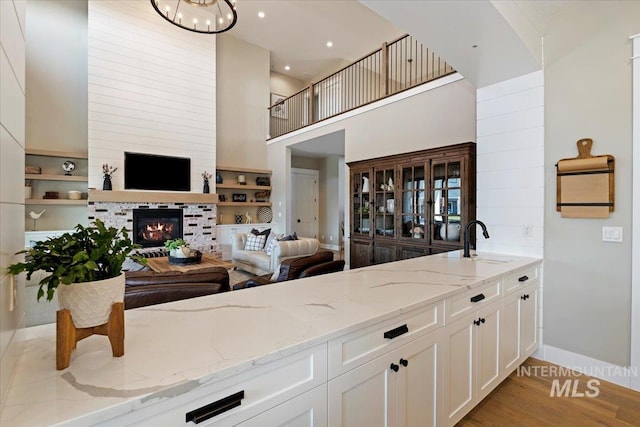 kitchen featuring white cabinetry, sink, light stone counters, a tiled fireplace, and light wood-type flooring