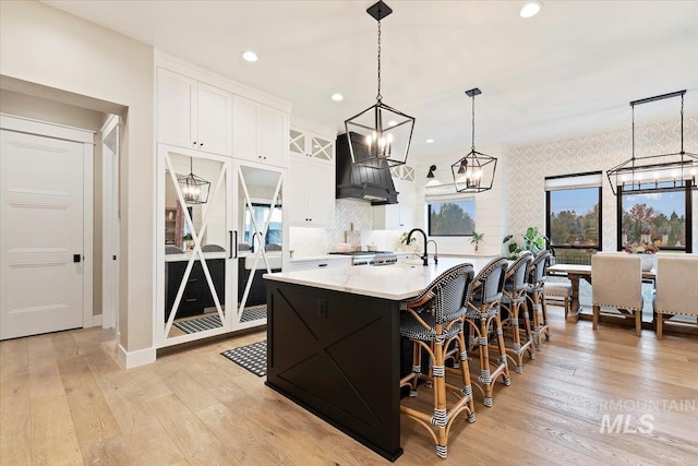 kitchen with a kitchen island with sink, light hardwood / wood-style flooring, white cabinets, and hanging light fixtures