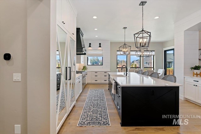 kitchen featuring a center island with sink, light hardwood / wood-style flooring, white cabinetry, and wall chimney range hood