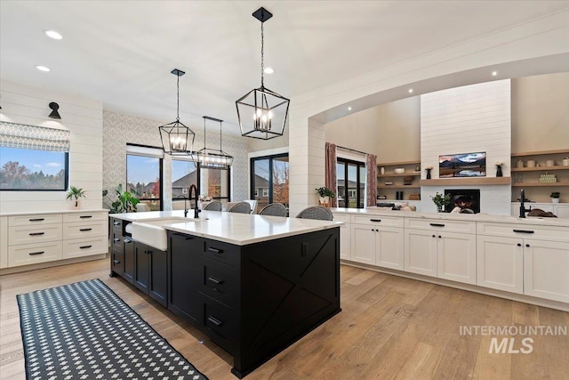 kitchen with sink, decorative light fixtures, a center island with sink, light hardwood / wood-style floors, and white cabinetry