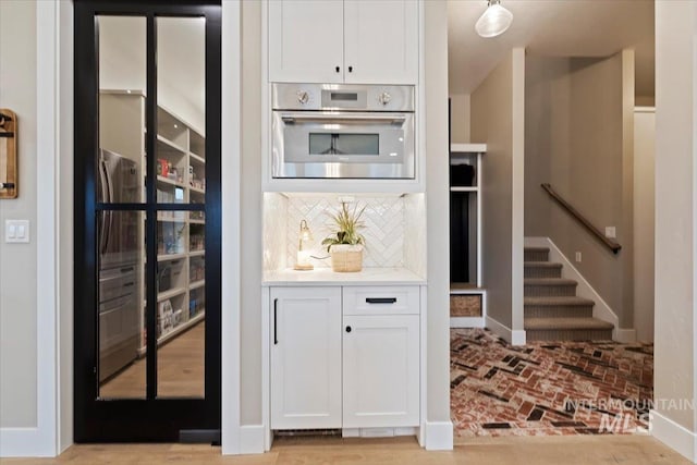 kitchen featuring white cabinets, oven, decorative light fixtures, and tasteful backsplash