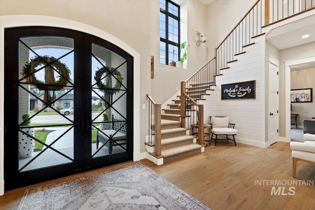 foyer featuring wooden walls, french doors, a towering ceiling, and light wood-type flooring