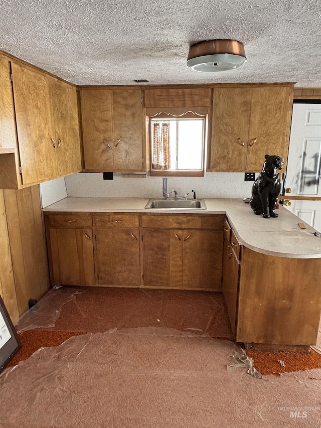 kitchen with a textured ceiling, light countertops, brown cabinetry, and a sink