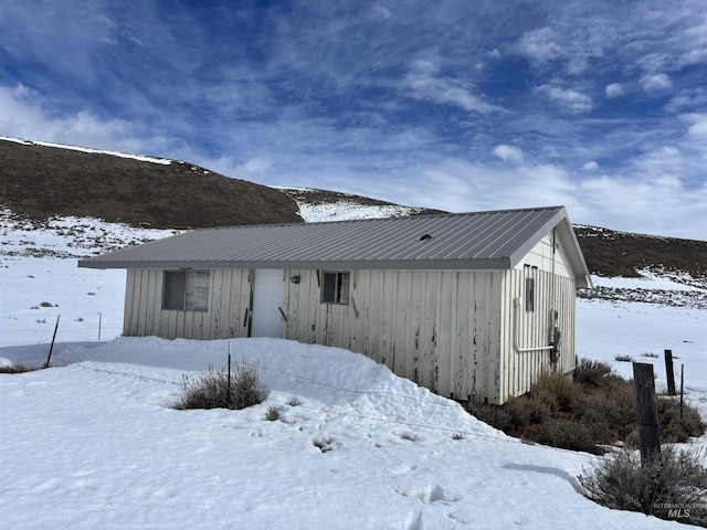 snow covered rear of property featuring board and batten siding and metal roof