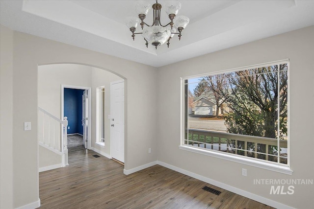 spare room featuring a chandelier, hardwood / wood-style floors, a raised ceiling, and plenty of natural light