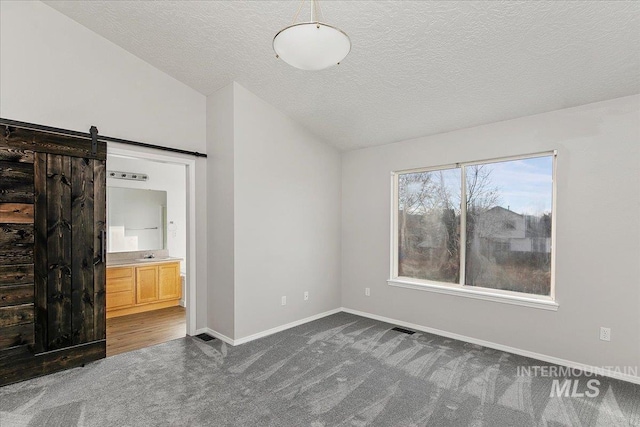 unfurnished bedroom with a textured ceiling, a barn door, dark carpet, and lofted ceiling