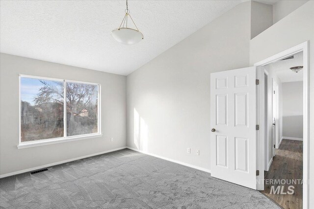 empty room with a textured ceiling, carpet floors, and vaulted ceiling