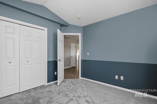 unfurnished bedroom featuring a textured ceiling, a closet, carpet floors, and vaulted ceiling