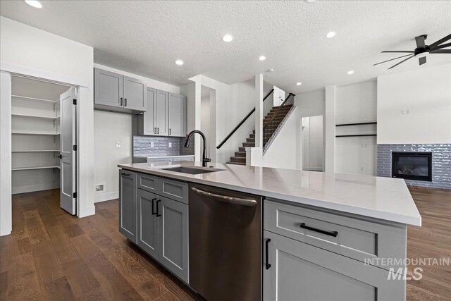 kitchen featuring dark hardwood / wood-style flooring, ceiling fan, stainless steel dishwasher, and an island with sink