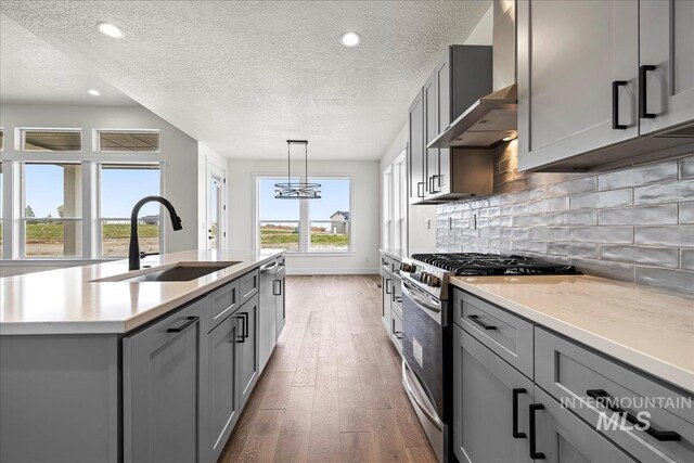 kitchen with decorative light fixtures, dark hardwood / wood-style floors, an island with sink, gas range, and sink