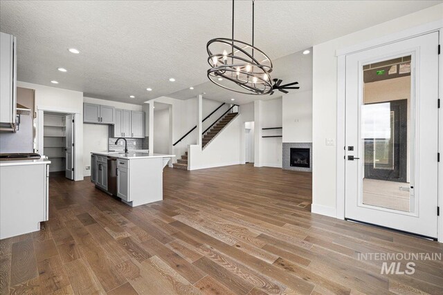 kitchen with stainless steel dishwasher, a center island with sink, a brick fireplace, and hardwood / wood-style flooring