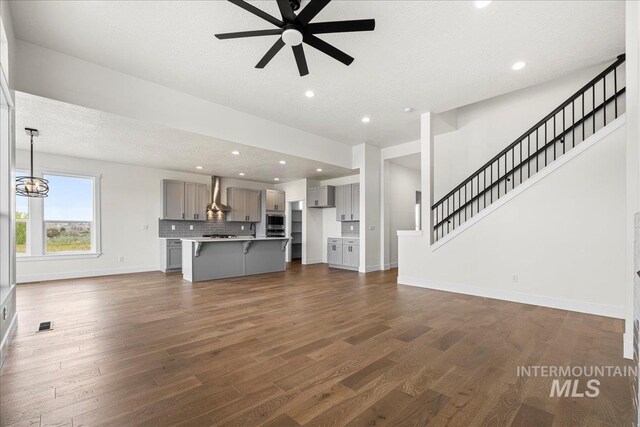 unfurnished living room with ceiling fan with notable chandelier, a textured ceiling, and dark hardwood / wood-style flooring