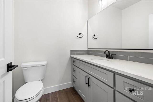 bathroom with hardwood / wood-style flooring, toilet, vanity, and backsplash