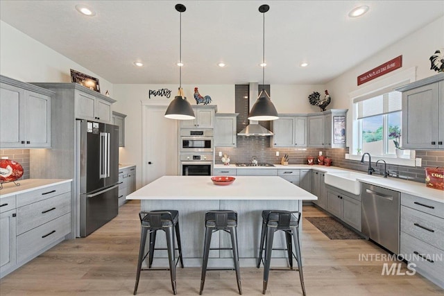 20150 Silver Spur Dr, Wilder, ID 83676 - kitchen featuring appliances with stainless steel finishes, gray cabinets, a breakfast bar, a center island, and wall chimney range hood