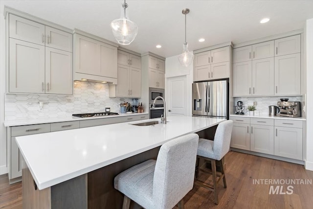 kitchen featuring dark wood-style floors, appliances with stainless steel finishes, a breakfast bar, light countertops, and a sink