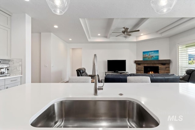 kitchen featuring a fireplace, tasteful backsplash, light countertops, open floor plan, and a sink