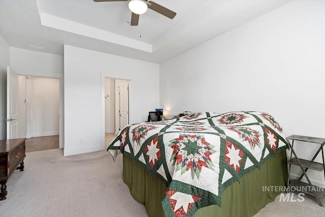 bedroom featuring a tray ceiling, light carpet, ceiling fan, and baseboards