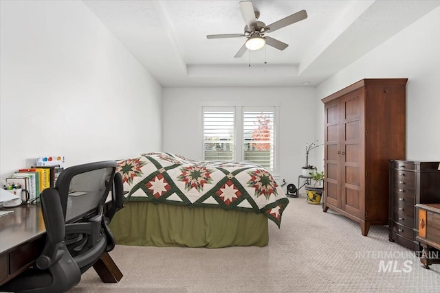 bedroom with light carpet, a raised ceiling, and a ceiling fan