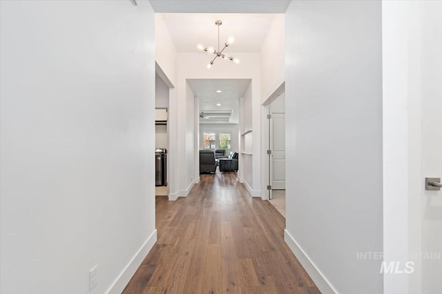 hallway with a notable chandelier, baseboards, and wood finished floors