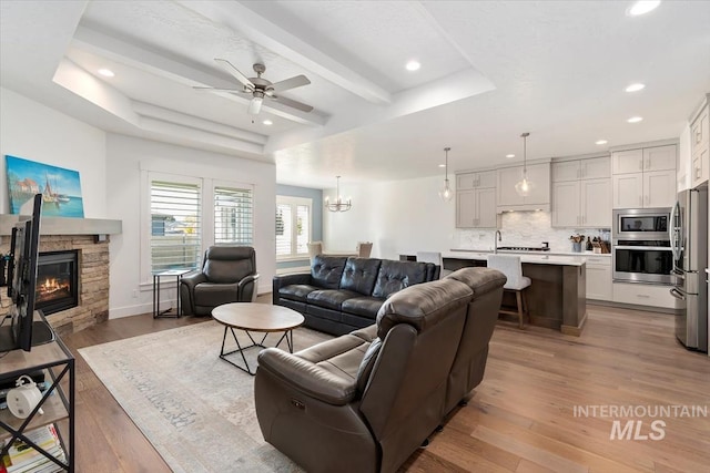 living area with recessed lighting, a raised ceiling, light wood-style flooring, and a stone fireplace