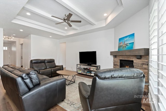 living area featuring a raised ceiling, a fireplace, beamed ceiling, and wood finished floors