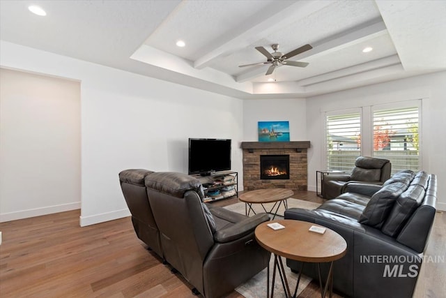 living area with light wood finished floors, a tray ceiling, a fireplace, and baseboards