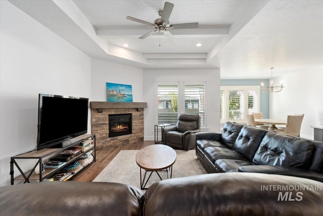 living area featuring recessed lighting, a raised ceiling, wood finished floors, a fireplace, and ceiling fan with notable chandelier