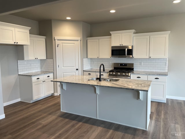 kitchen with baseboards, a sink, an island with sink, and stainless steel appliances