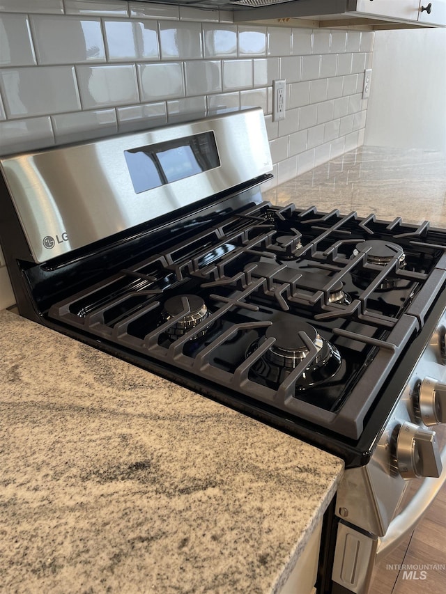 interior details with stainless steel range with gas stovetop, light stone countertops, and tasteful backsplash