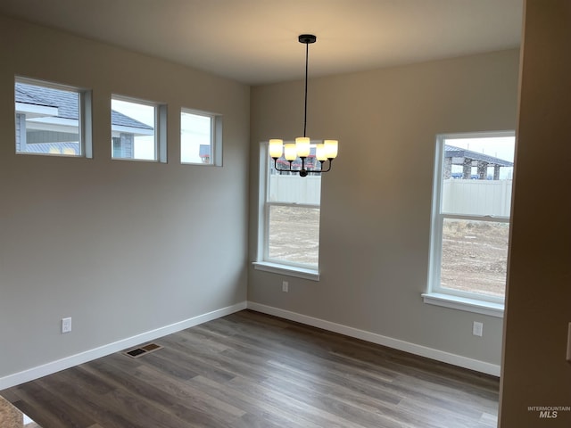unfurnished dining area featuring a healthy amount of sunlight, dark wood finished floors, and a notable chandelier