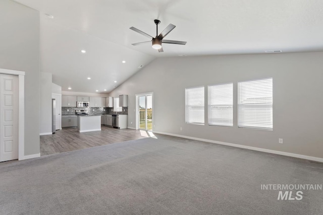 unfurnished living room with vaulted ceiling, light carpet, and ceiling fan