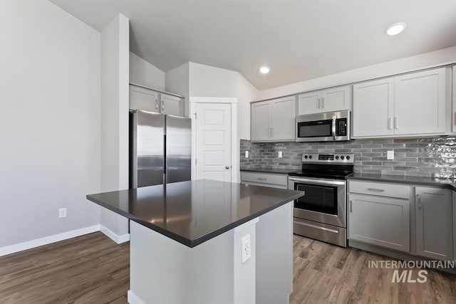 kitchen with appliances with stainless steel finishes, wood-type flooring, vaulted ceiling, and decorative backsplash