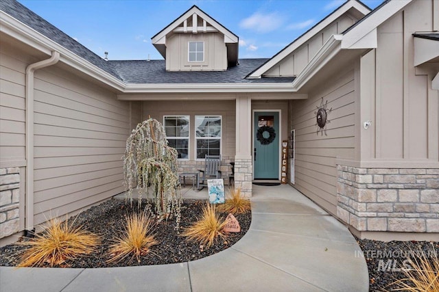 view of exterior entry featuring a shingled roof, stone siding, and board and batten siding