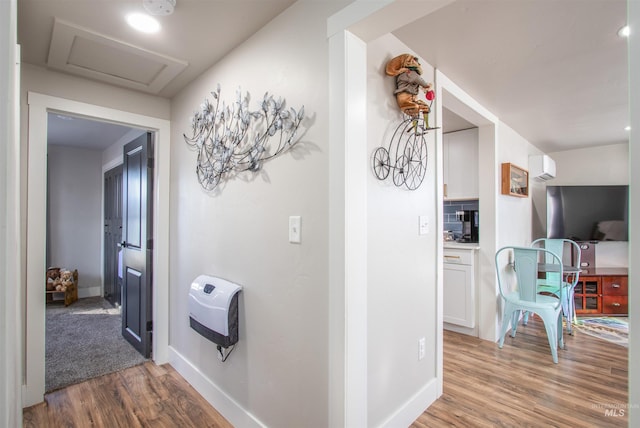 corridor featuring attic access, baseboards, wood finished floors, a wall mounted air conditioner, and heating unit