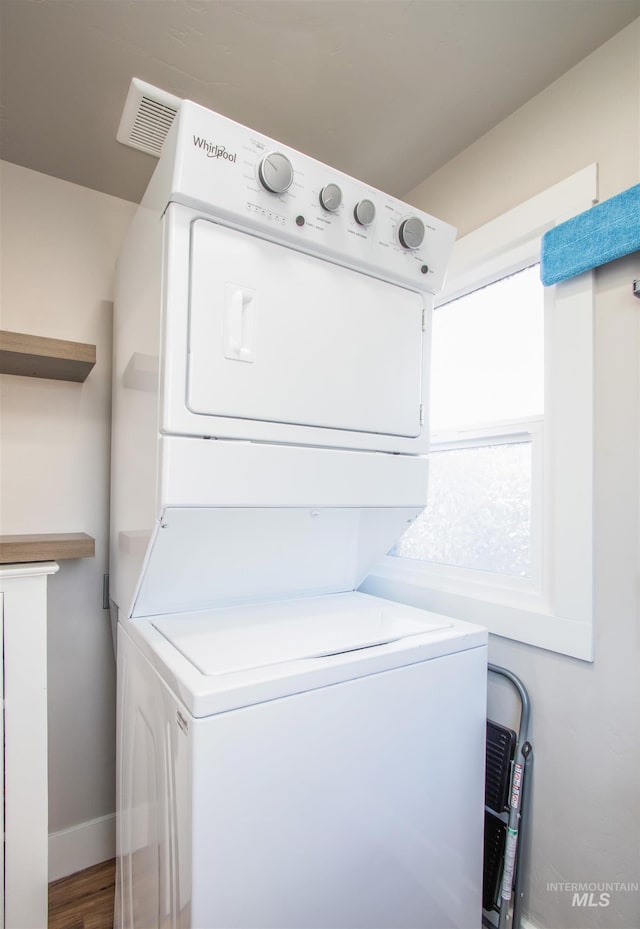 clothes washing area featuring laundry area, baseboards, a wealth of natural light, and stacked washer / dryer