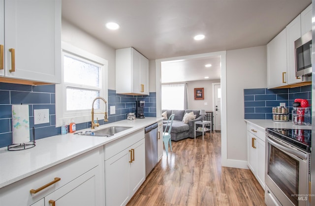 kitchen with a sink, light countertops, appliances with stainless steel finishes, light wood-type flooring, and a wealth of natural light