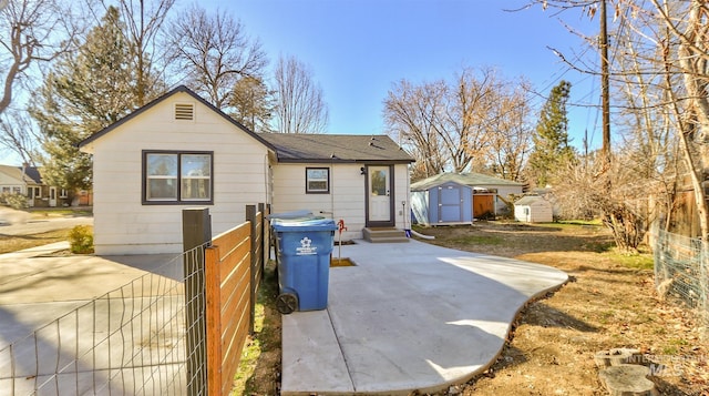 back of house with entry steps, a shingled roof, an outdoor structure, a shed, and a patio area