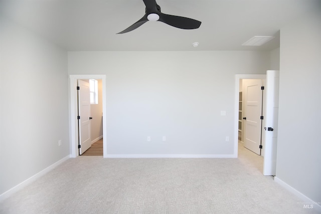 unfurnished bedroom with baseboards, light colored carpet, ensuite bath, ceiling fan, and a spacious closet