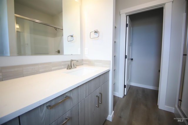 full bathroom with wood finished floors, vanity, baseboards, a shower, and backsplash