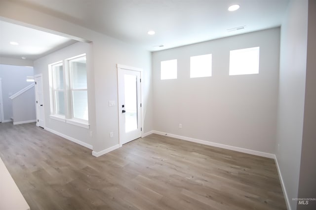 unfurnished room featuring recessed lighting, wood finished floors, visible vents, baseboards, and stairway