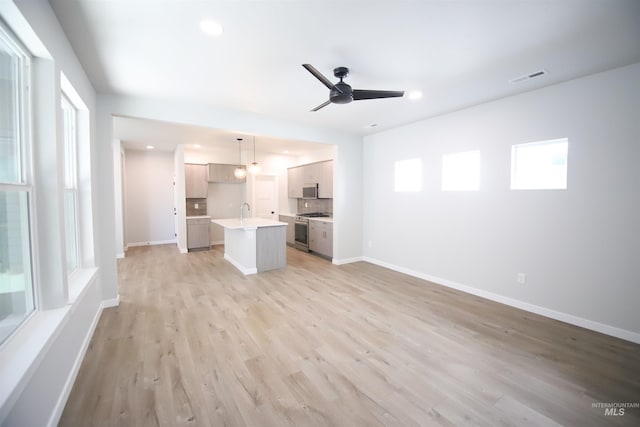 unfurnished living room featuring ceiling fan, a sink, visible vents, baseboards, and light wood-style floors