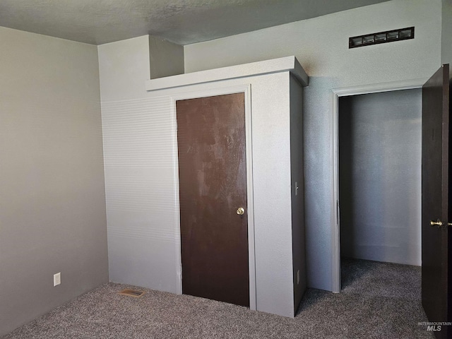 unfurnished bedroom with dark colored carpet, a textured ceiling, and a closet