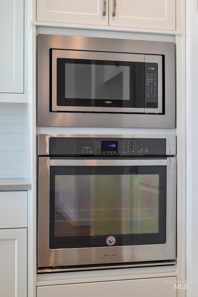 details with decorative backsplash, white cabinetry, and stainless steel microwave