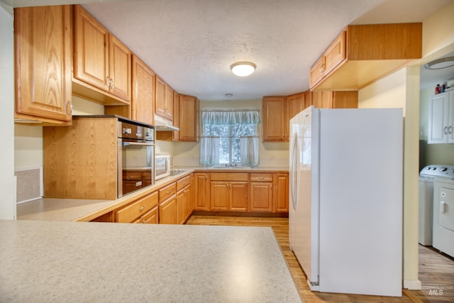 kitchen with light wood-type flooring, a textured ceiling, white appliances, sink, and washer / clothes dryer